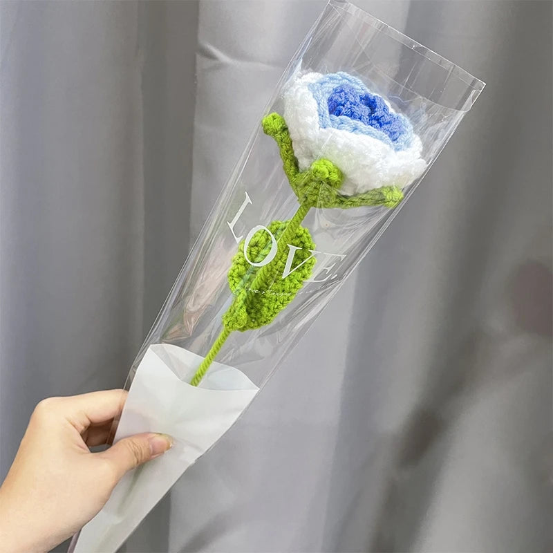 A handmade crochet tulip bouquet featuring blue and white flowers is displayed inside a clear plastic sleeve.