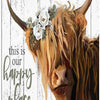A close-up painting of a Highland cow's head with horns and a floral wreath, set against a distressed white wooden background