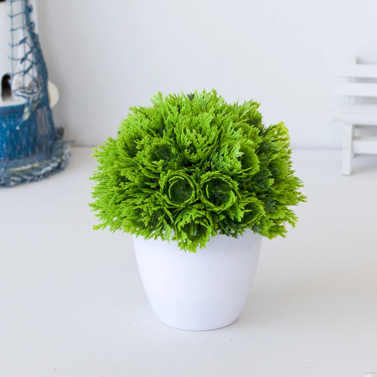 Un vibrant plant de bonsaï artificiel vert dans un pot blanc sur une surface blanche.