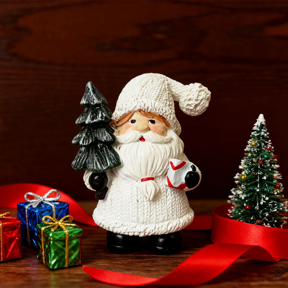 Adorno navideño de Papá Noel de punto blanco con barba y sombrero, sobre una superficie de madera con cinta roja y verde navi