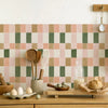 A kitchen backsplash featuring a retro pattern of pink and olive green square tiles, with wooden kitchen items displayed belo