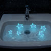 A white bathroom sink filled with glowing blue water featuring sea turtle light decorations.