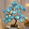 Sculpture d'arbre sombre en forme de roses bleues avec lumières LED, sur une table blanche.