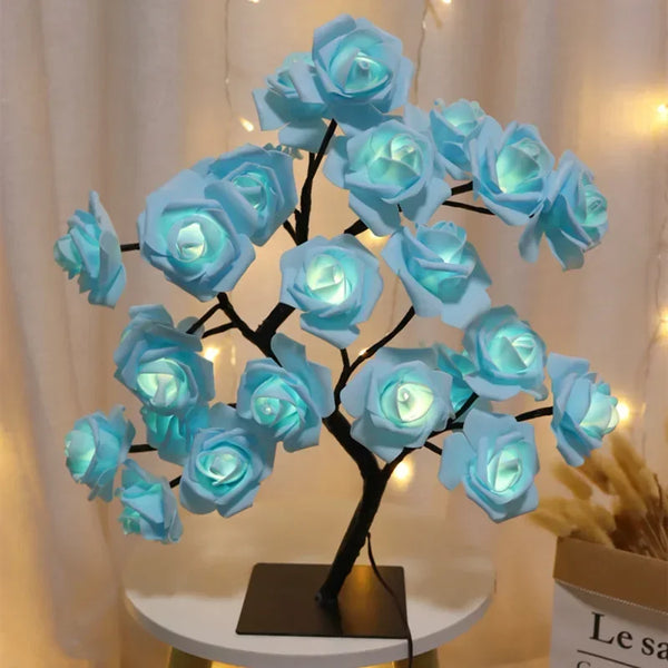 Escultura de árbol oscuro con forma de rosas azules y luces LED brillantes sobre una mesa blanca.