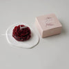 A handcrafted rose-shaped scented candle in a pink box and on a white plate.