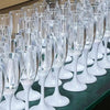 Une rangée de verres à boire en verre transparent avec des pieds et des bases blancs, disposés sur une surface vert foncé.