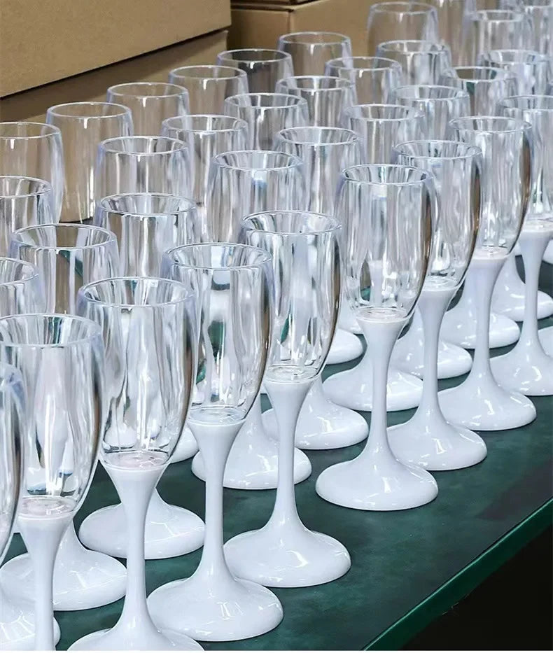 Une rangée de verres à boire en verre transparent avec des pieds et des bases blancs, disposés sur une surface vert foncé.