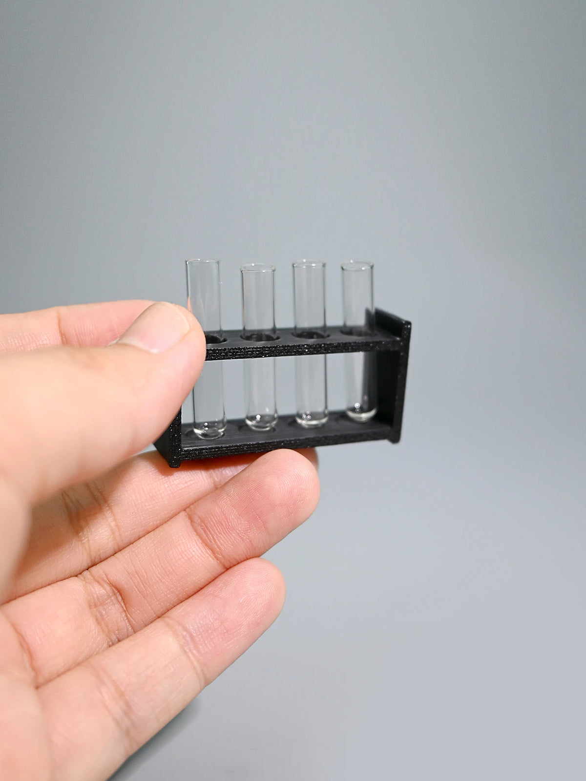 A hand holds a black miniature laboratory set with five clear glass tubes for dollhouse or photography