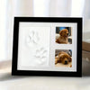 A black photo frame displaying white paw print molds and two photographs of a golden retriever dog.