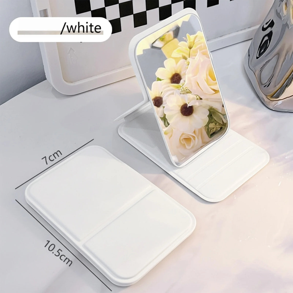 A white portable folding HD makeup mirror is shown with a floral arrangement on a light surface.