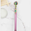 A pair of iridescent pink and green stainless steel candle wick trimmer scissors resting on a white marble surface.
