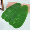 A set of five green tropical banana leaf coasters resting on a light wooden surface.