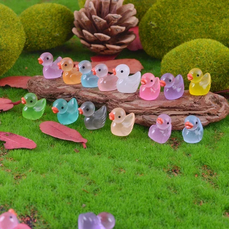 A collection of luminous mini duck figurines in various pastel colors resting on mossy green grass with pinecones and leaves.