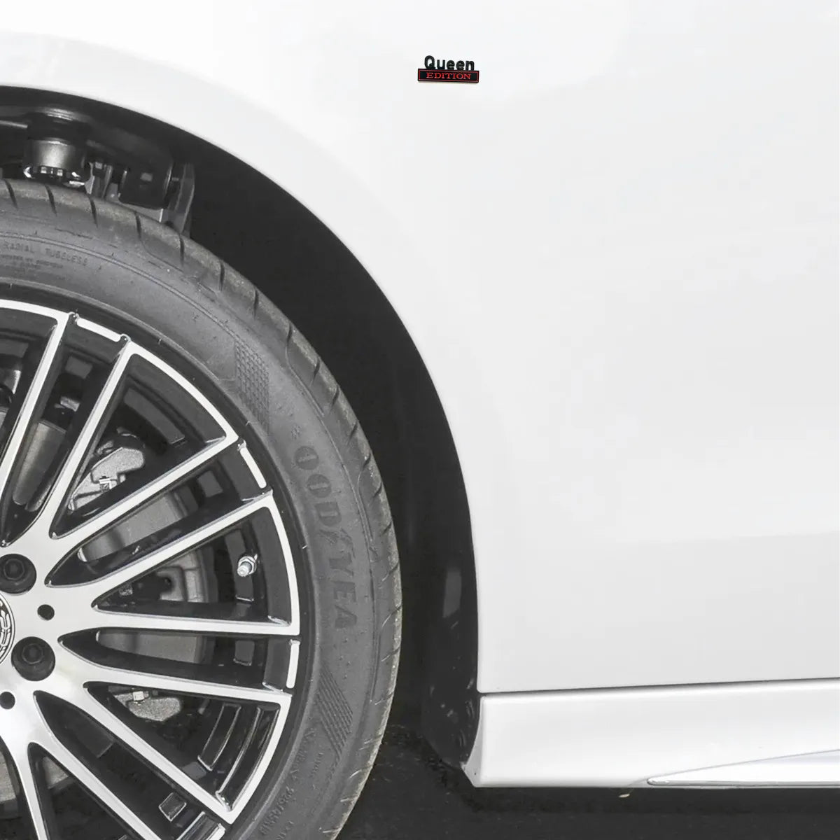 Nahaufnahme eines weißen Auto-Rades mit schwarzem Leichtmetallfelge und Reifen, das ein Queen Edition Emblem-Aufkleber zeigt.