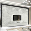 A modern interior featuring a large wall panel with a white leaf pattern and a black frame, displaying a mounted television.