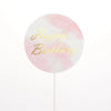 A round pink watercolor design with gold text that reads Happy Birthday on a white stick.