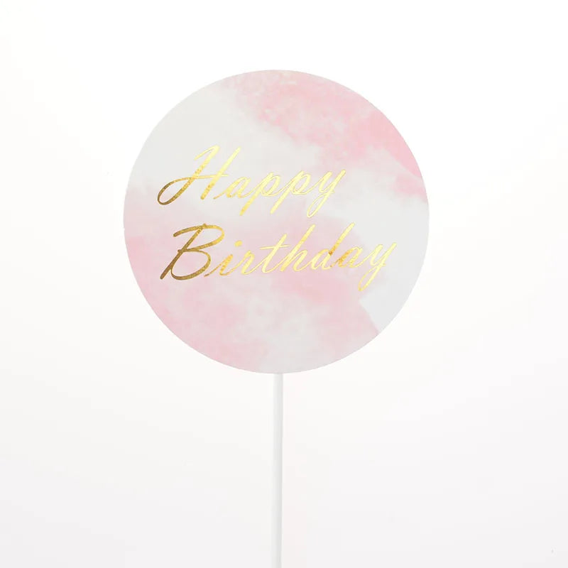 A round pink watercolor design with gold text that reads Happy Birthday on a white stick.
