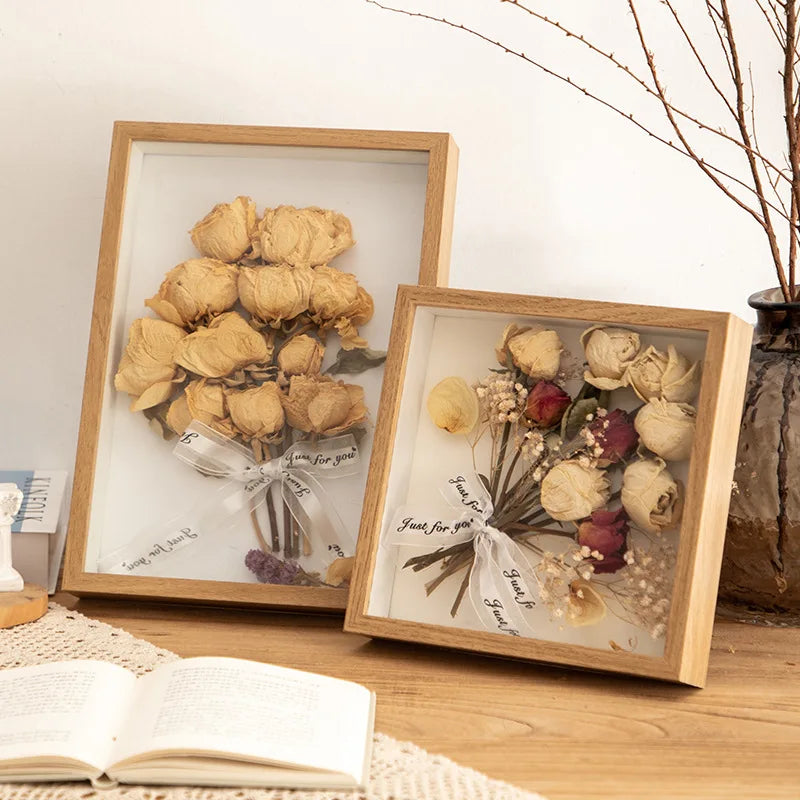 A wooden shadow box photo frame containing dried beige flowers tied with a white ribbon.