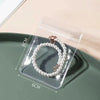 A clear plastic storage bag holds a pearl necklace on a green tray.