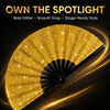 A close-up of a gold glitter hand fan opening to reveal a bright, sparkling surface.