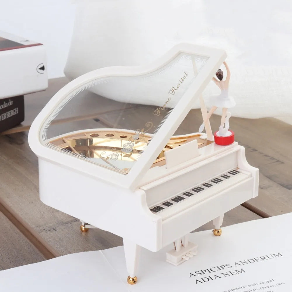A white hand-crank music box featuring a ballerina with a spinning top, displayed on a wooden surface.