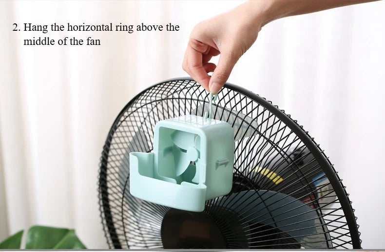 A hand is hanging a horizontal ring above the middle of a black portable ice-cooling floor fan.