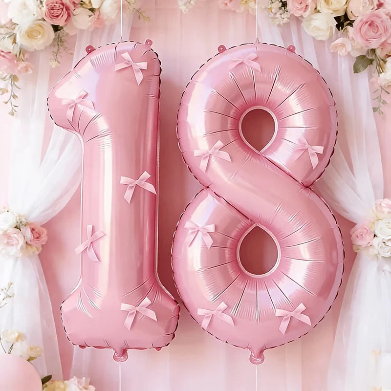 Two pink foil number balloons, one '1' and one '8', are suspended against a soft pink background with floral decorations.