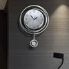 A modern circular wall clock with silver casing and Arabic numerals mounted on a dark gray textured wall.