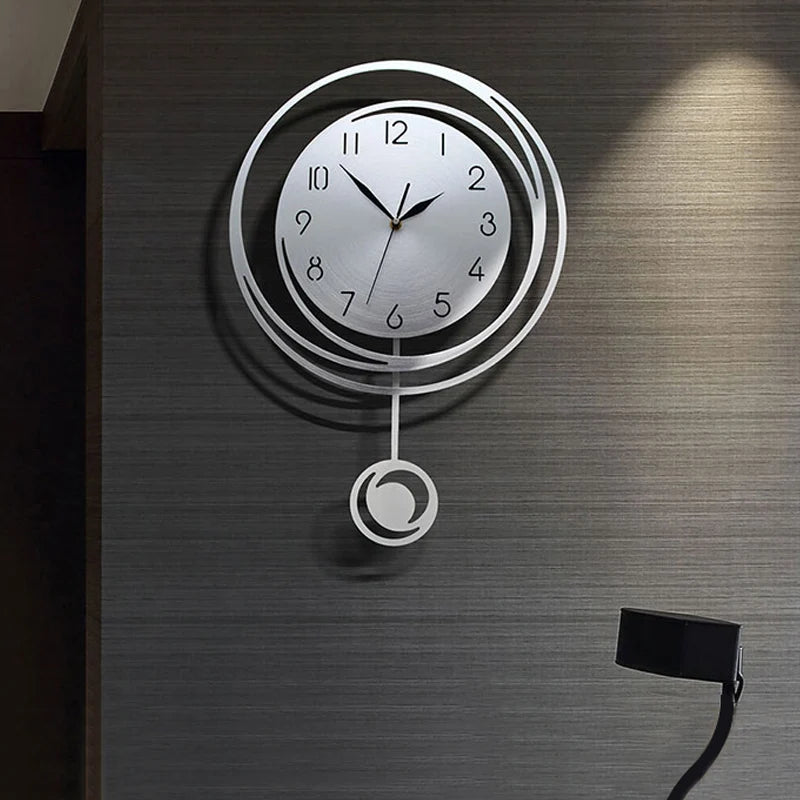 A modern circular wall clock with silver casing and Arabic numerals mounted on a dark gray textured wall.