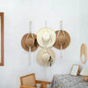 Boho wall hanging featuring three macrame hat organizers with wooden dowels mounted on a white wall.