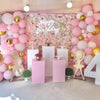A pink and gold balloon garland arch decorated with confetti and a Happy Birthday sign for a celebration.