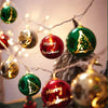 A festive holiday decoration featuring green and red ornaments hanging from fairy lights.