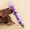 A long, tapered crystal point featuring purple amethyst and white patterns, resting on a piece of driftwood.