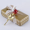 Rote Glaskristallrose-Dekoration mit durchsichtiger Schleife auf einer goldenen Geschenkbox.