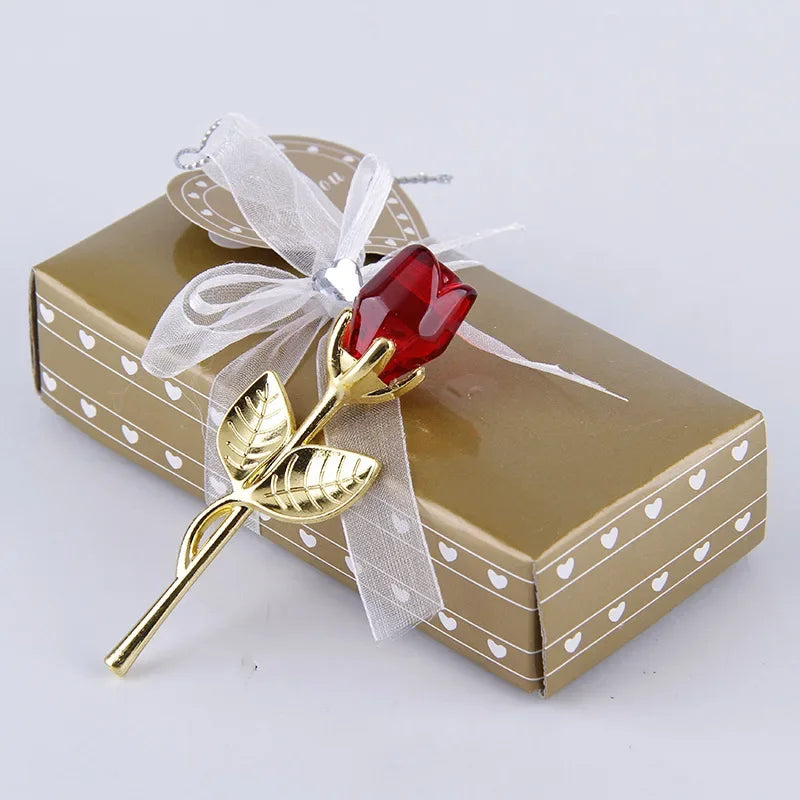 Rote Glaskristallrose-Dekoration mit durchsichtiger Schleife auf einer goldenen Geschenkbox.