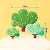 A set of three green tree cake toppers with brown trunks and leaves on a white cake.