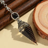 A dark brown crystal pendulum with a silver chain and decorative finial rests on a wooden board.