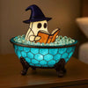A ceramic ghost figurine with a witch hat is sitting in a blue glass bowl filled with clear stones, illuminated by an LED lig