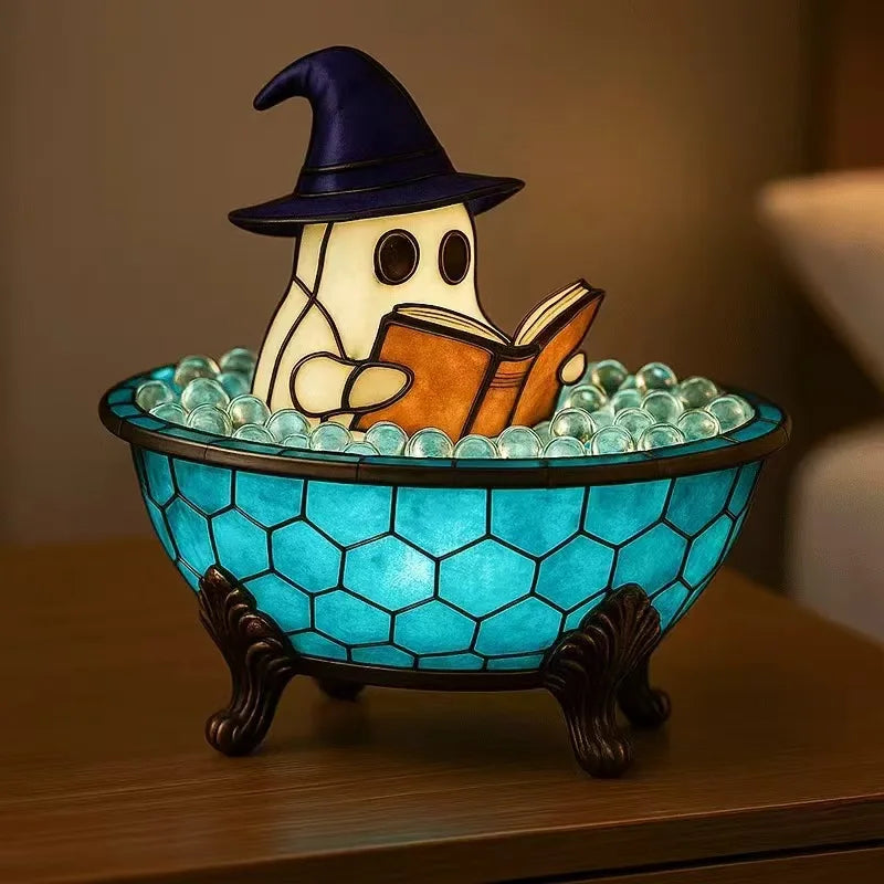 A ceramic ghost figurine with a witch hat is sitting in a blue glass bowl filled with clear stones, illuminated by an LED lig