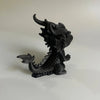 A black 3D printed mini dragon statue collectible sitting on a white surface.