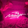 A neon sign spelling out The Midnight glows pink against a textured magenta background with soft lighting.