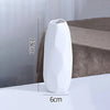 A white ceramic bud vase with a smooth, elongated shape is shown on a surface.