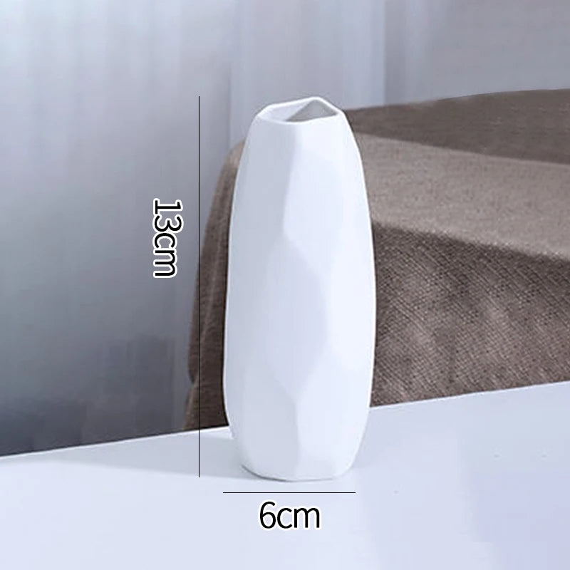 A white ceramic bud vase with a smooth, elongated shape is shown on a surface.