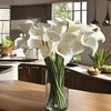 A bouquet of five white calla lily stems in a glass vase on a wooden table.