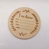A round wooden sign with a wreath border and the text I'm here, intended for newborn hospital keepsakes.