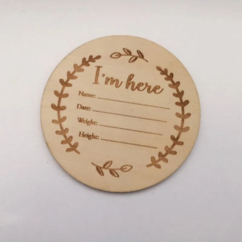 A round wooden sign with a wreath border and the text I'm here, intended for newborn hospital keepsakes.