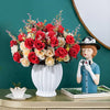 A vibrant bouquet of artificial silk red and cream roses in a white vase on a wooden surface.