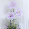 A cluster of large artificial silk purple poppy flowers on a stand against a white background.