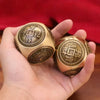 A hand holds two antique-style Chinese lucky coins, featuring traditional characters and a square design, against a red backg