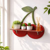 A red wooden wall shelf holds potted plants and a glass jar with thin wooden sticks.